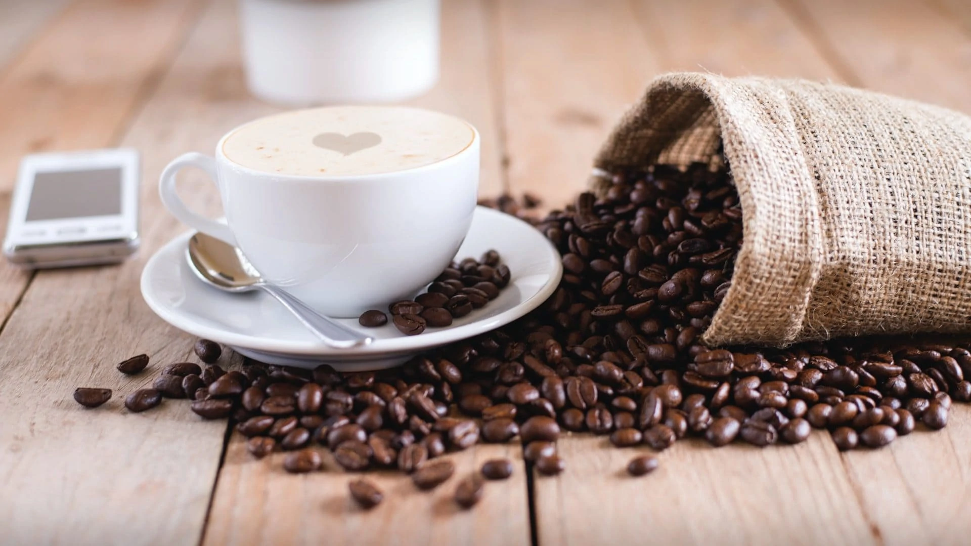 Kop koffie met zak bonen ernaast, op houten ondergrond. Vooraanzicht