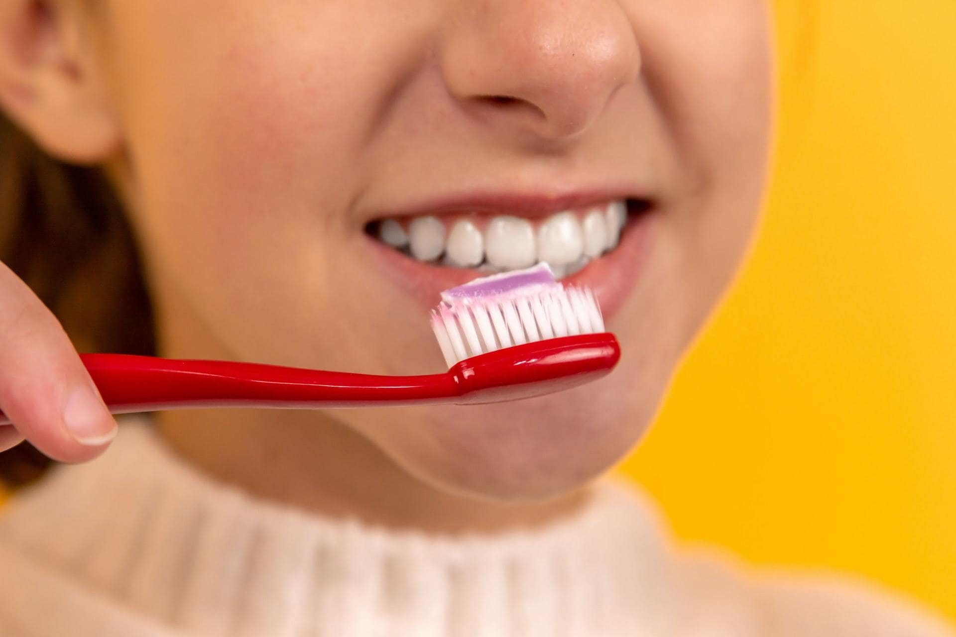 Persoon met witte tanden die tandenborstel vast houdt, op gele achtergrond