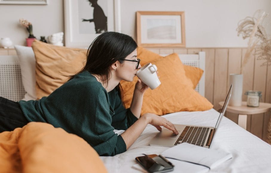Vrouw op bed met kop koffie en laptop