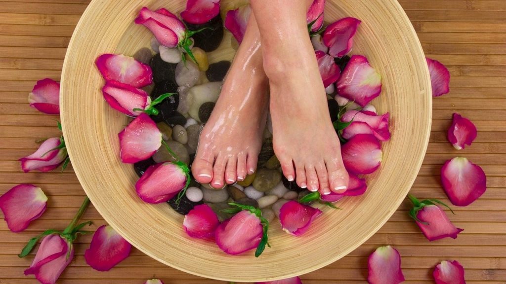Vrouwen voeten in een voetenbad met stenen en rozenblaadjes.