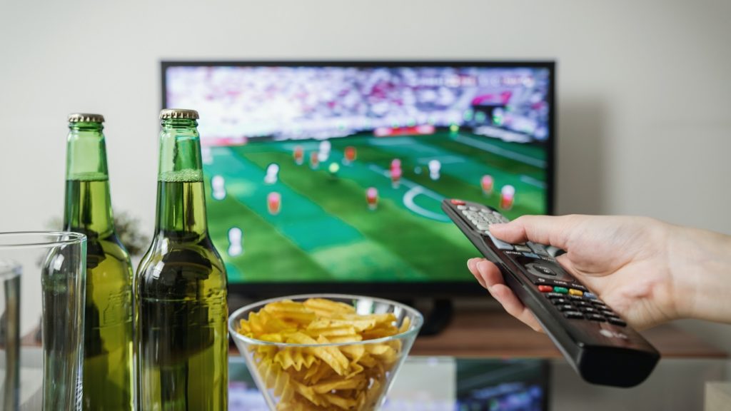 Bakje chips met twee flesjes bier en hand met afstandbediening voor tv