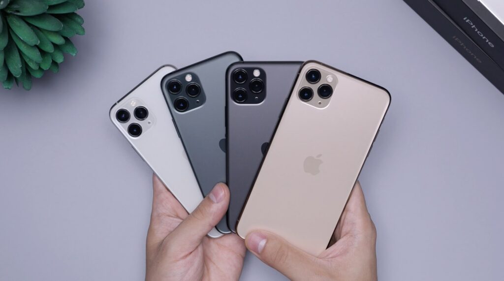 Vier verschillende iPhones in twee handen op zachtroze achtergrond, bovenaanzicht.