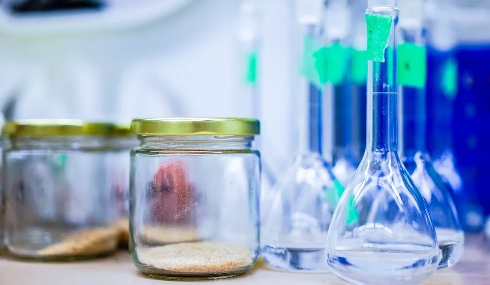 Glazen potjes met poeder naast erlenmeyr flessen in een lab 