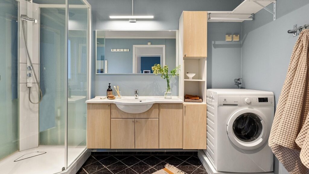Blauw/zwarte badkamer met houte kasten, links een douche en rechts een wasmachine