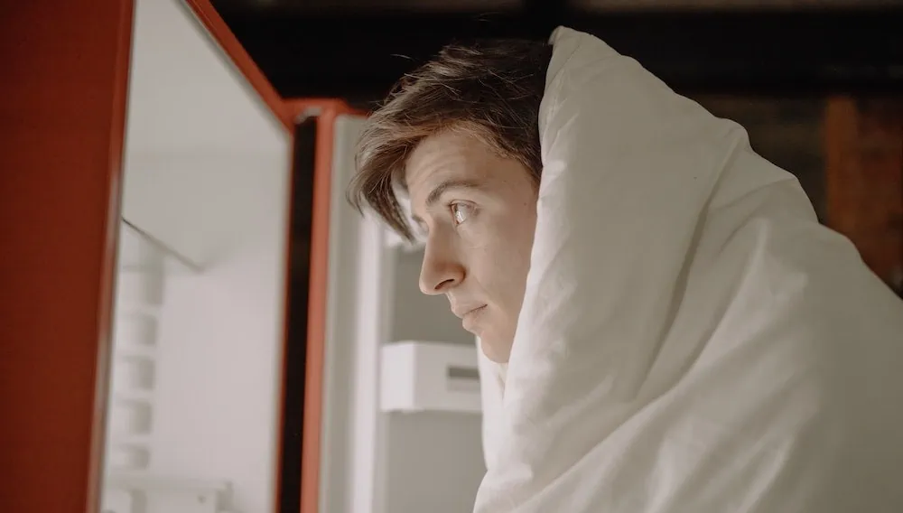 jongen in deken staat voor open koelkast